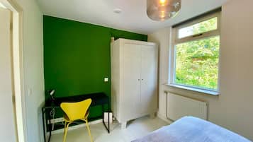 Une chambre à coucher comprenant un lit, une armoire, un bureau avec une chaise, une fenêtre donnant sur un espace verdoyant et un luminaire suspendu.