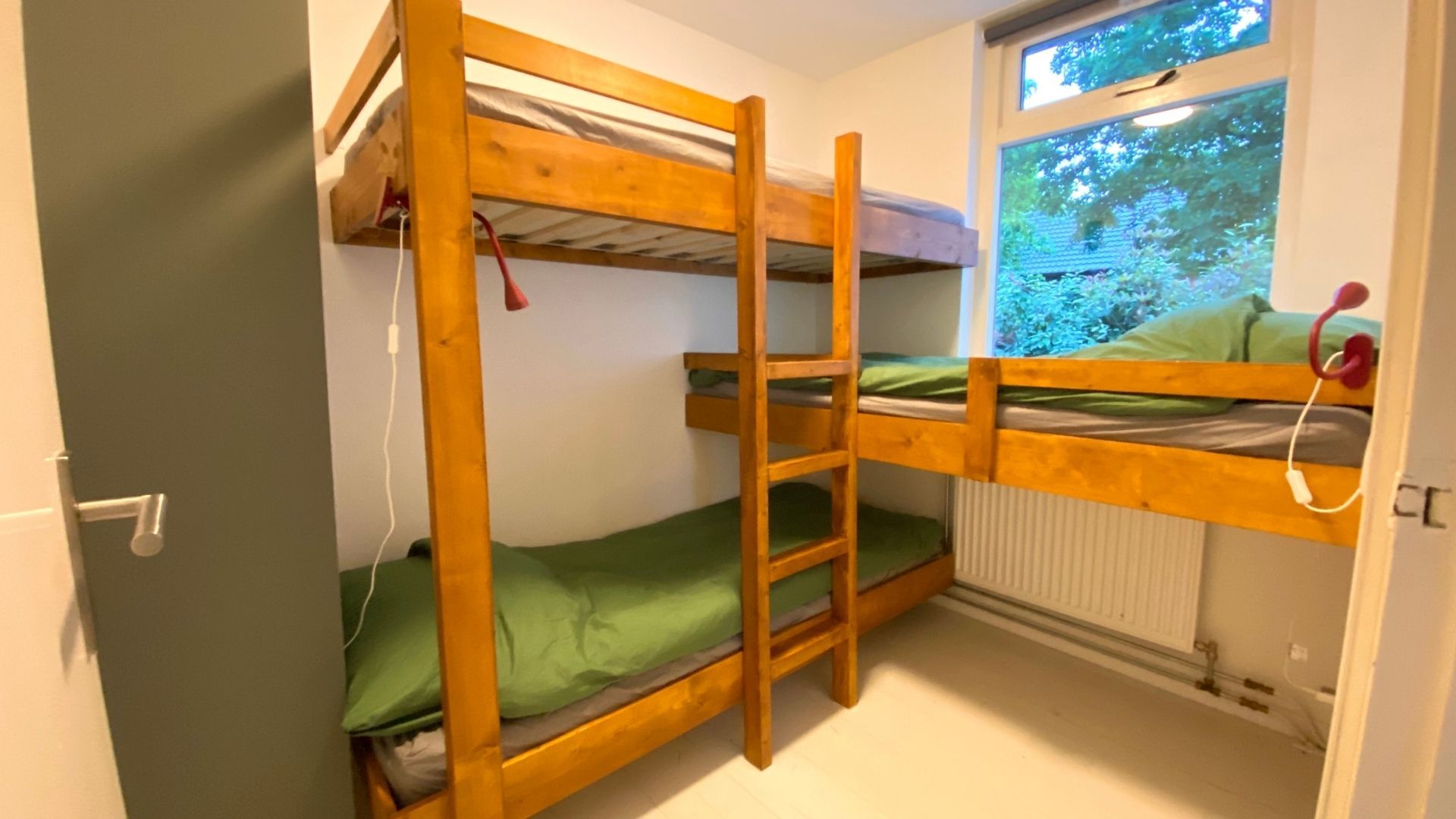 Une chambre avec un lit superposé, une fenêtre, un radiateur et une porte.