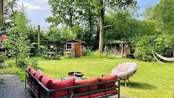 Un giardino con un divano rosso, un'amaca e una piccola costruzione in legno.