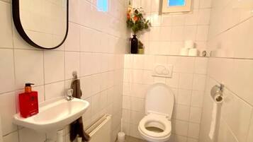 Un bagno piccolo e pulito, rivestito di piastrelle bianche, con un lavandino bianco, un water, uno specchio e un piccolo oblò.