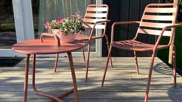 A patio with a round table and two chairs, a potted plant, and a wooden deck.