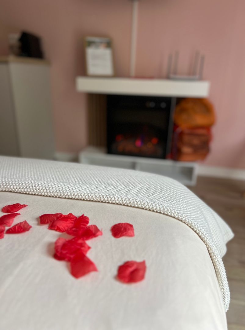 Un letto con una coperta bianca e petali di rosa rossa sparsi.