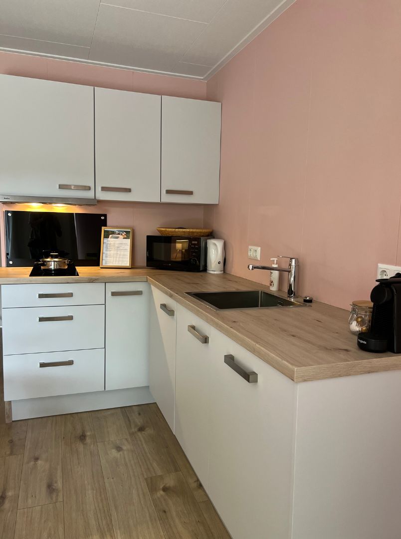 Une cuisine compacte avec des meubles blancs, un plan de travail en bois, un évier, un four à micro-ondes et une bouilloire.