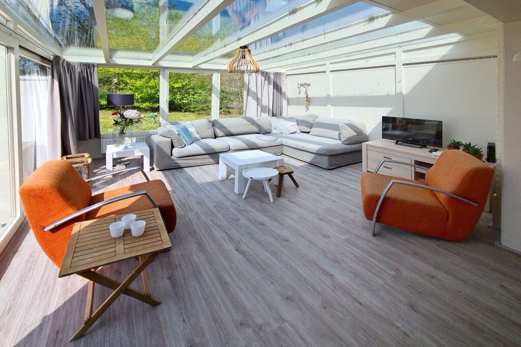 Uma sala de estar moderna com teto de vidro, sofá modular, duas poltronas, mesa de centro e televisão.