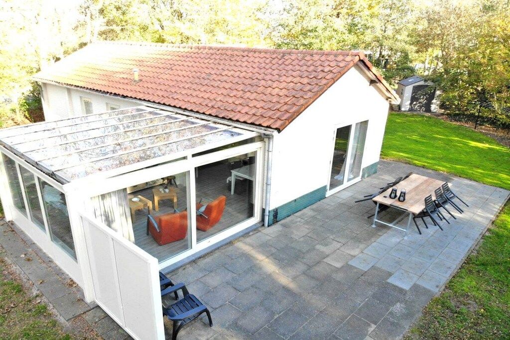 Une maison dotée d’un patio entièrement vitré, d’un coin repas avec une table et des chaises, et d’un toit recouvert de tuiles rouges.