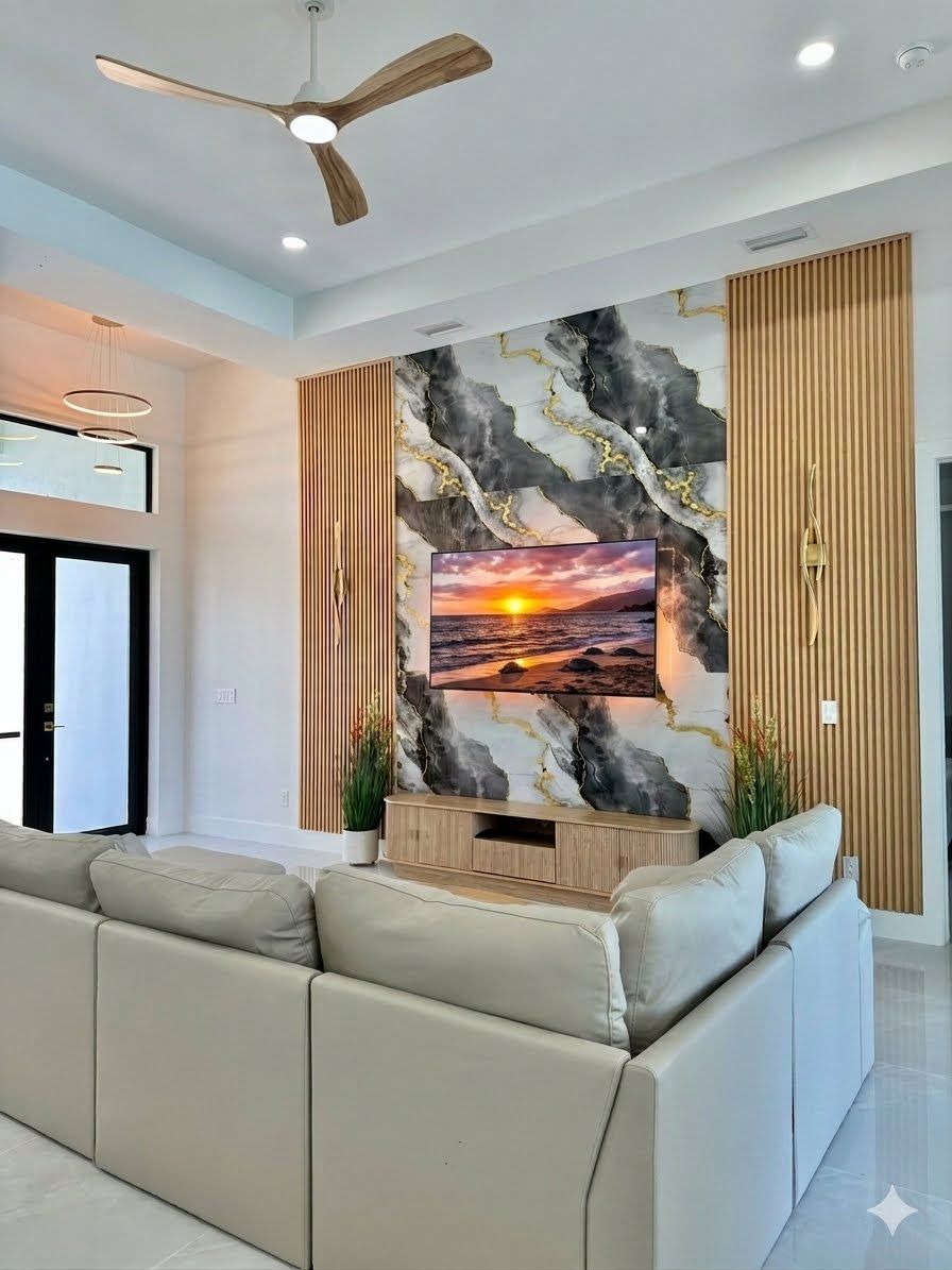 Una sala moderna con un sofá grande, un ventilador de techo y un televisor de pared que muestra una escena de atardecer.