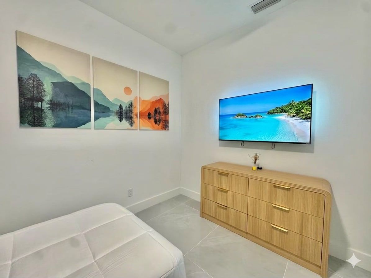 Une chambre avec un lit, un téléviseur fixé au mur et une armoire en bois.