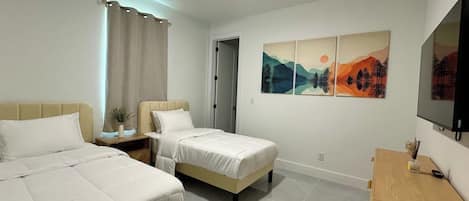 Habitación de hotel con dos camas, ventilador de techo, televisor y obras de arte en la pared.
