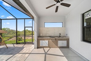 A modern outdoor kitchen with a ceiling fan, a window, and a view of the landscape. - Canal Life-Private Pool-Tropical Florida Escape (Cape Coral)