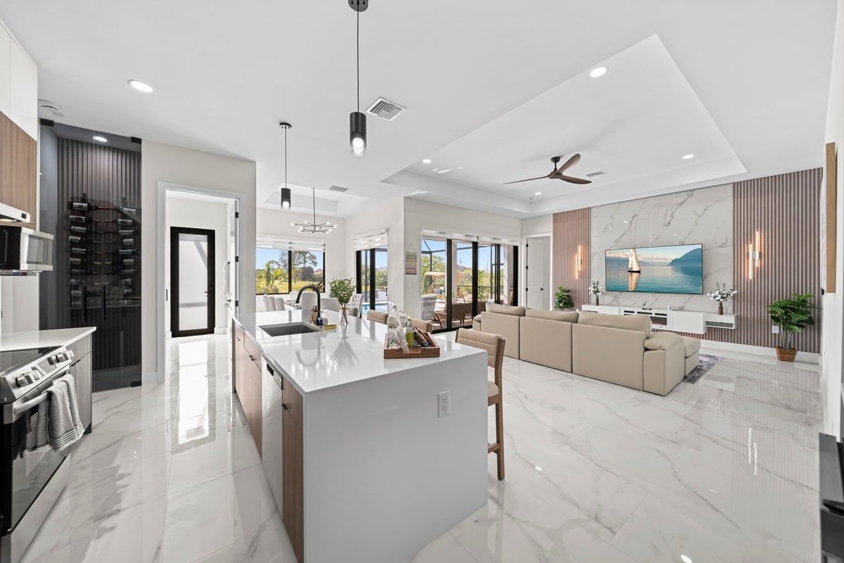 A modern kitchen with a central island, a dining area with a sofa, and a living room with a TV and a large window.