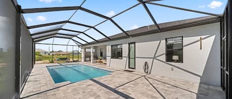 A covered outdoor swimming pool area with a geometric roof structure, a pool, and a patio with seating.