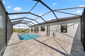 Ein überdachter Poolbereich im Freien mit einer geometrischen Dachkonstruktion, einem Schwimmbecken und einer Terrasse mit Sitzmöglichkeiten.