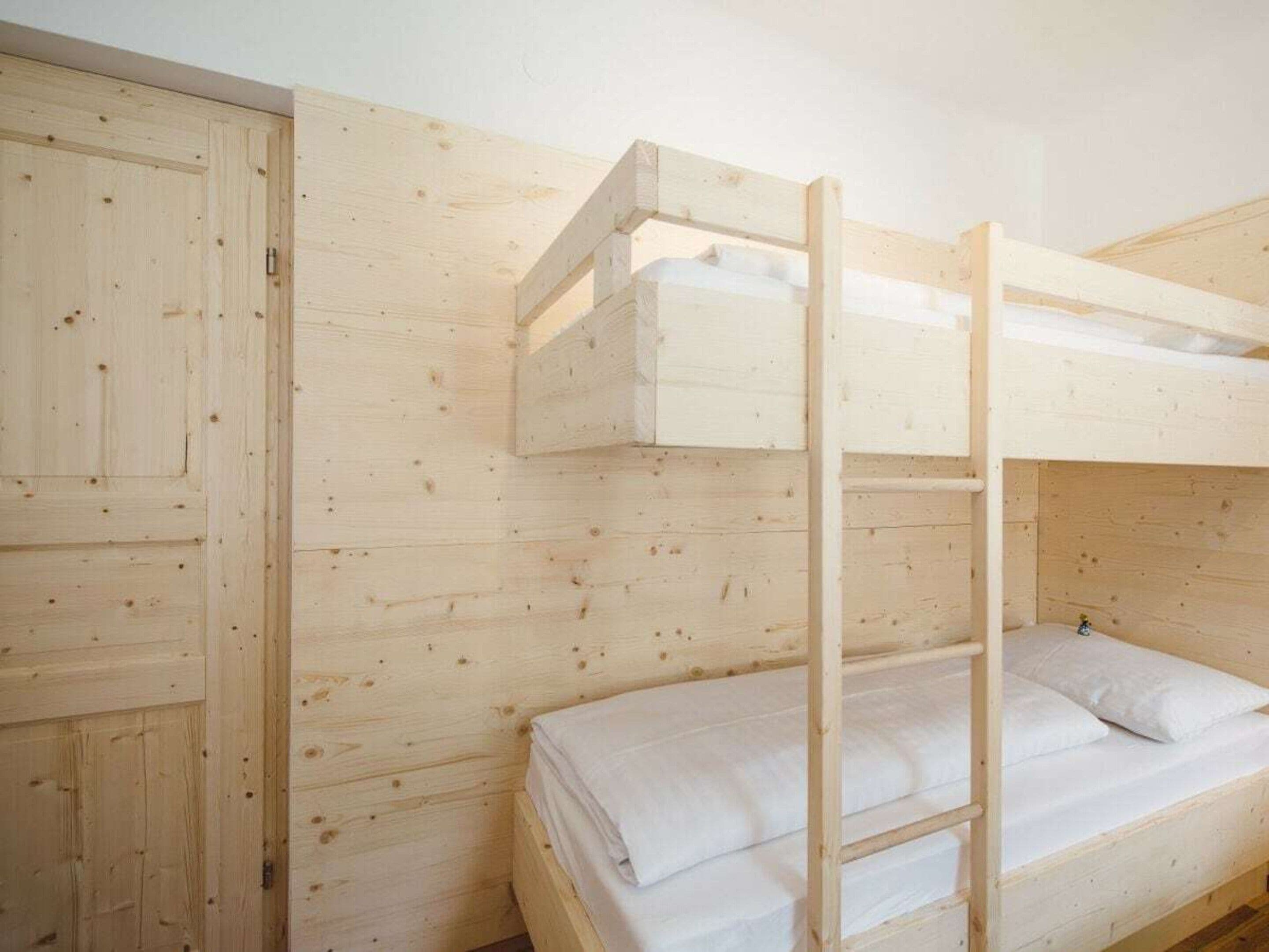 Een stapelbed met een ladder, een houten garderobe en een effen muur.