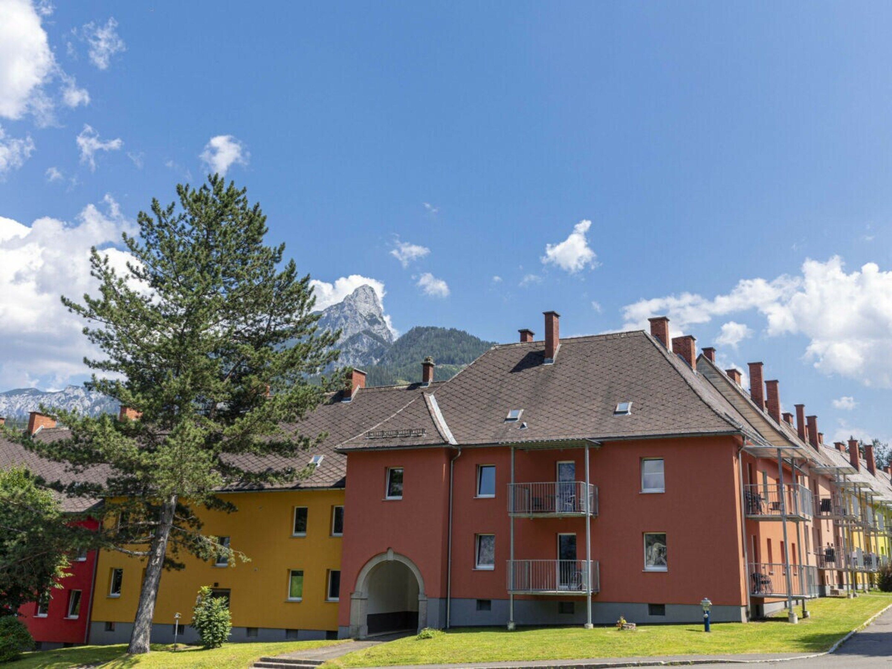 A row of multi-story buildings with balconies, set against a backdrop of mountains and a clear sky.