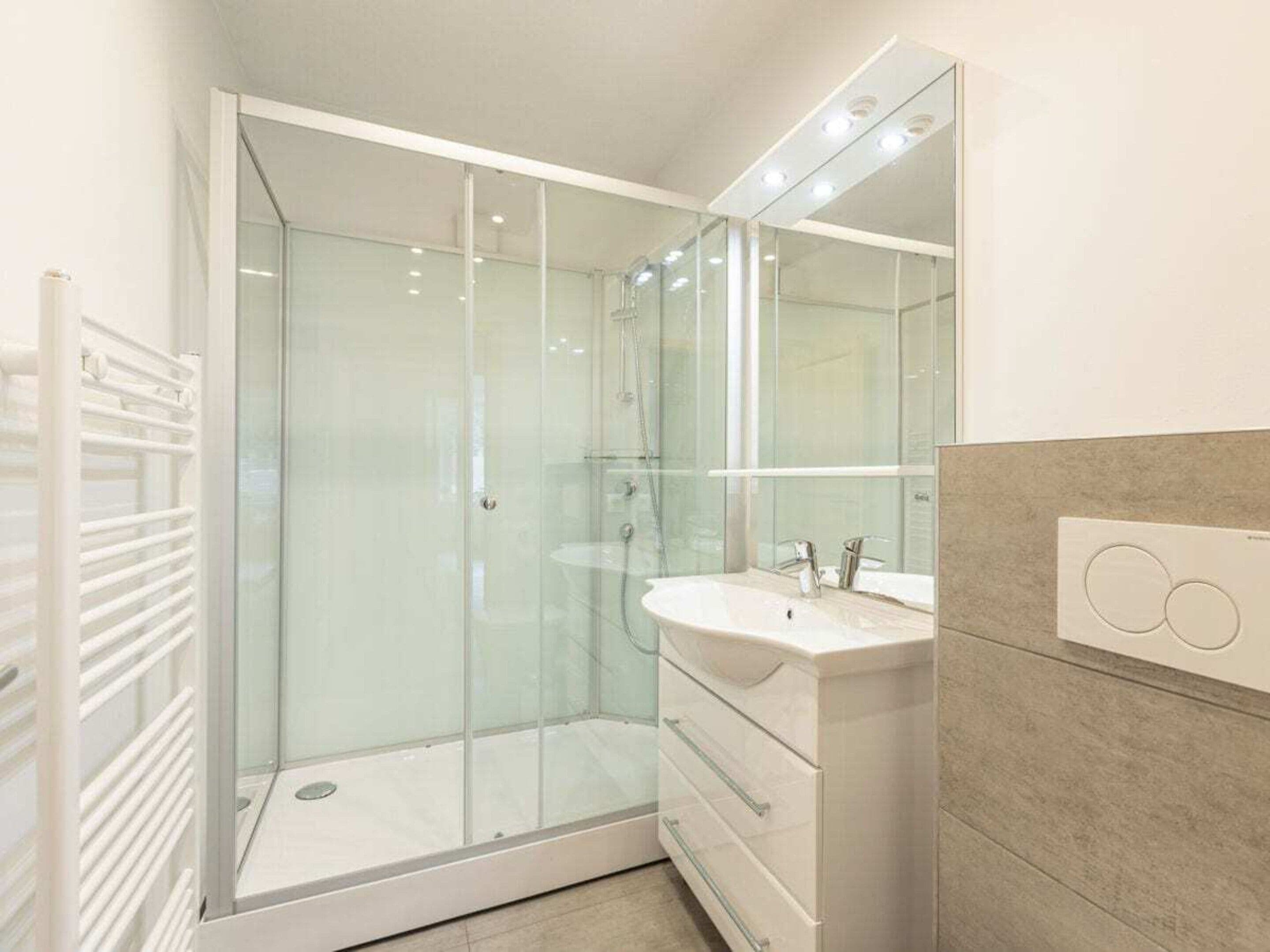 A modern bathroom with a glass-enclosed shower, a white vanity with a sink, and a large mirror.
