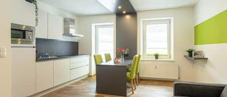 A modern kitchen with white cabinets, a built-in microwave, and a dining area with a table and chairs.