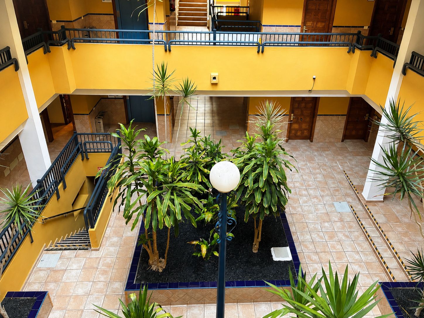 Un atrio de varios niveles con un jardín central, múltiples escaleras y una decoración en tonos amarillo y blanco.
