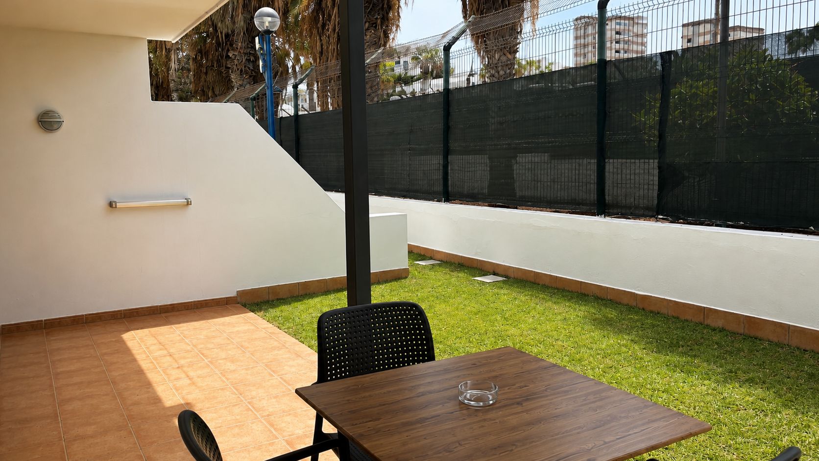 Un patio con una mesa, sillas, un pequeño césped y una cerca.