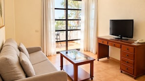A living room with a sofa, a glass-top coffee table, a wooden desk with a television, and a telephone.