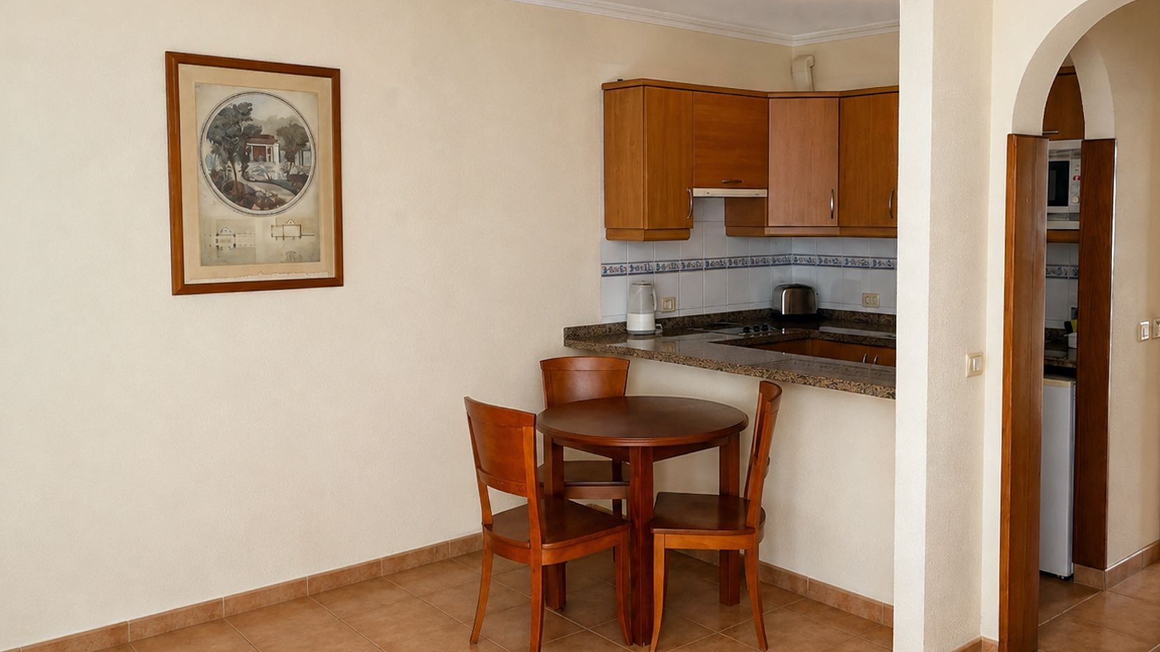Una cocina pequeña con armarios de madera, encimera de granito y una mesa de comedor con sillas.