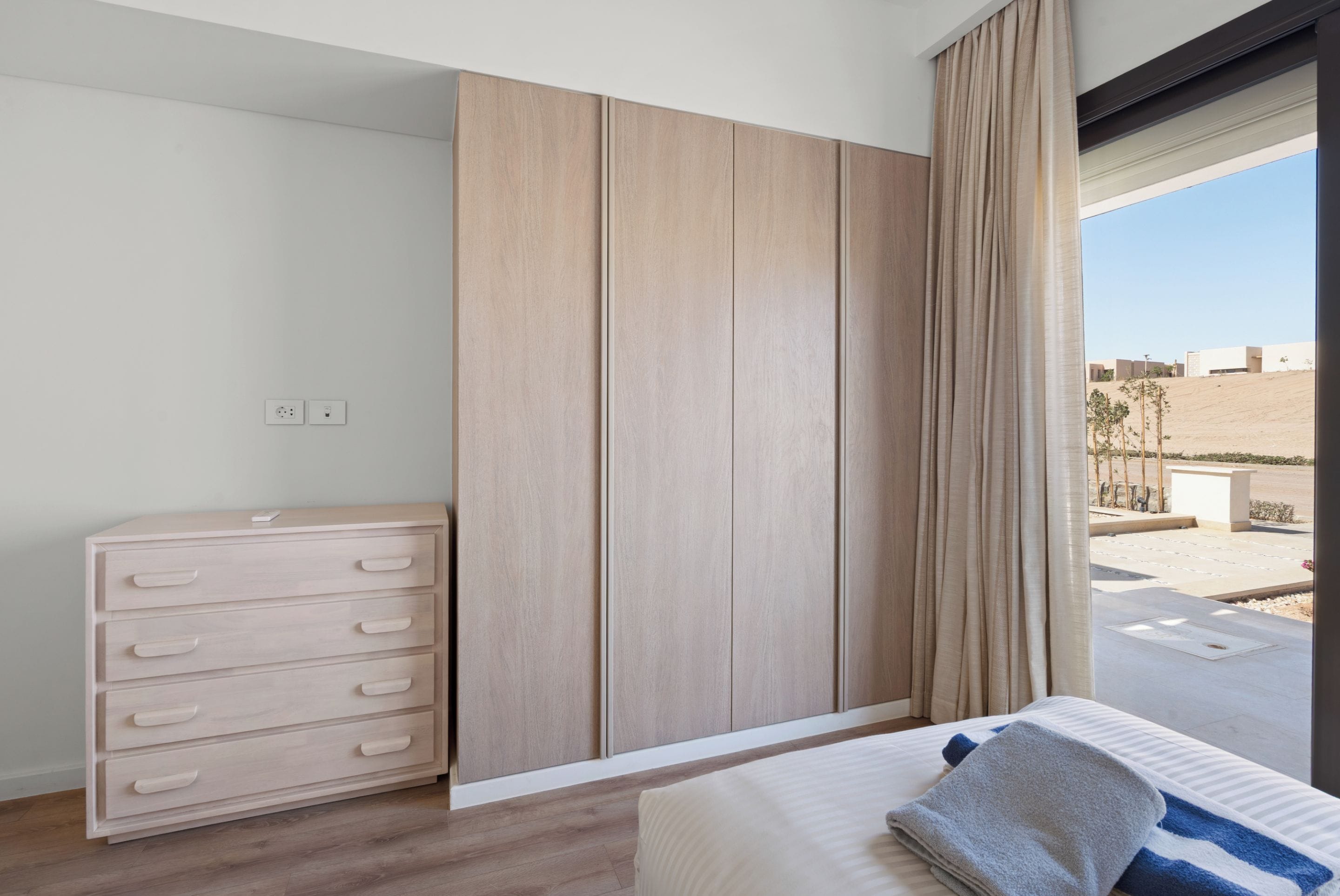 Ein Schlafzimmer mit Bett, Kommode, Kleiderschrank und Blick nach draußen.