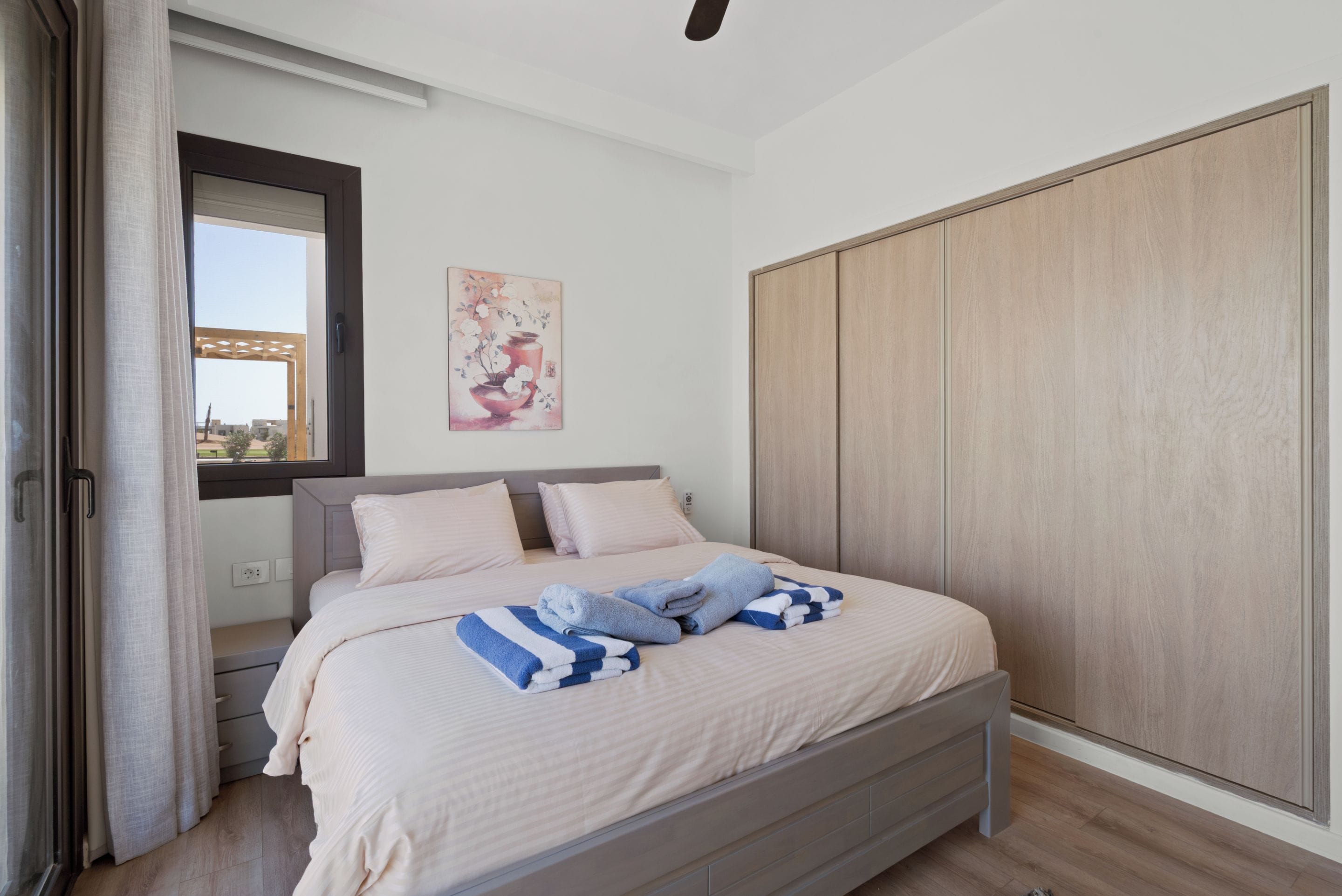 Une chambre à coucher avec un lit, une armoire, une fenêtre avec des rideaux et un tableau accroché au mur.
