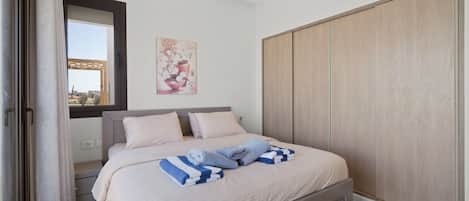 Un dormitorio con cama, armario, ventana con cortinas y un cuadro en la pared.
