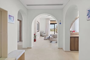 A modern interior with a hallway leading to a living area, featuring a stone wall, a sofa, and a dining area. - Designer Golf Villa -Pool & Serene Views (El Gouna)