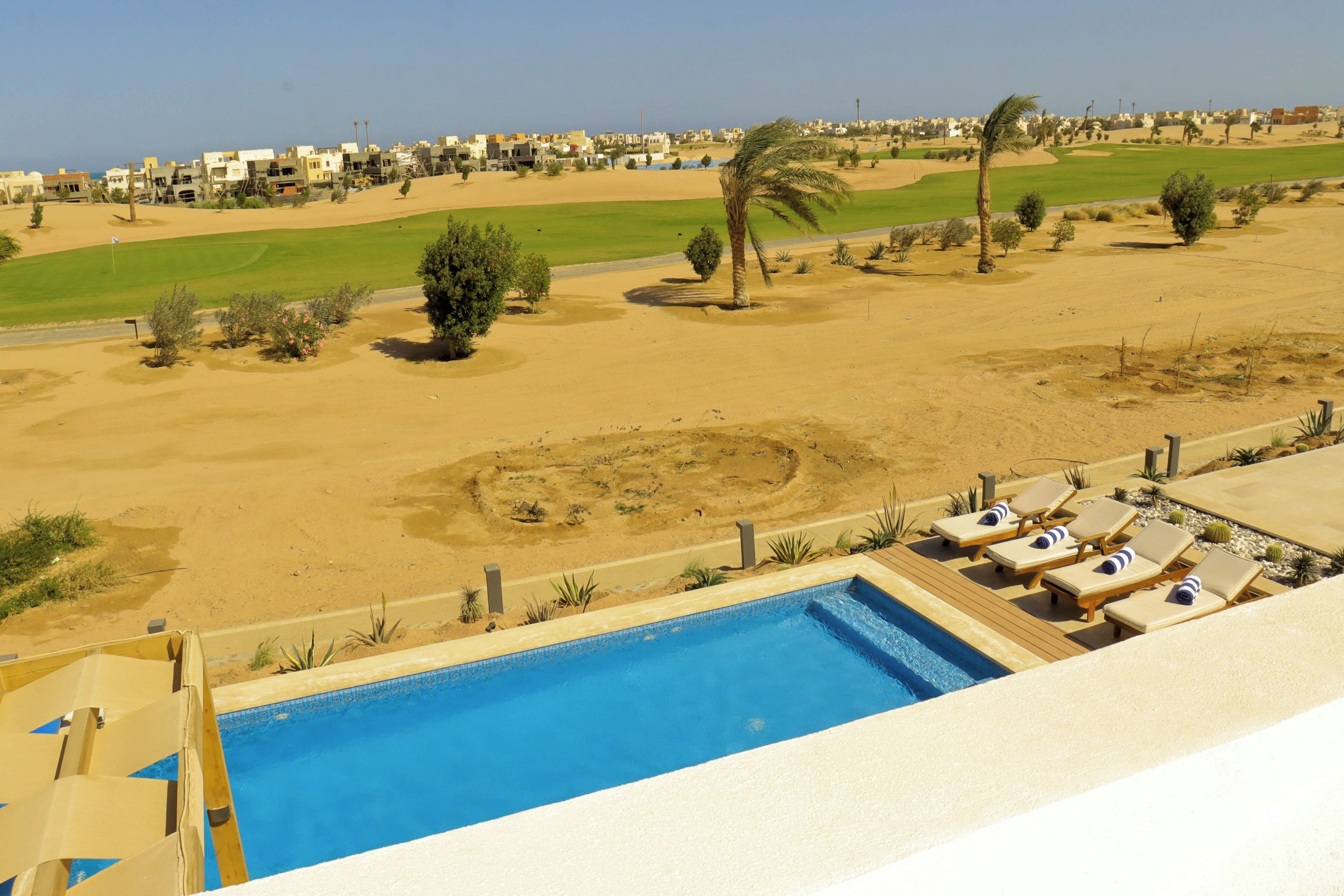A pool area with a view of a desert landscape and a golf course in the background.