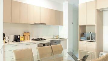A modern kitchen with light wood cabinets, a gas stove, a dishwasher, and a dining area with a glass table and chairs.