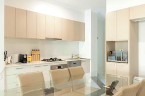 Een moderne keuken met lichte houten kastjes, een gasfornuis, een vaatwasser en een eethoek met een glazen tafel en stoelen.