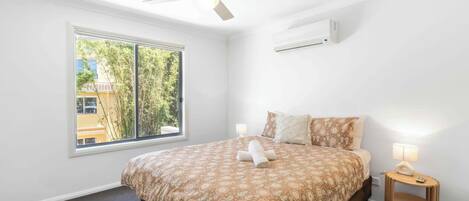 Ein Schlafzimmer mit einem Bett, einem Deckenventilator, einem Fenster und einem Nachttisch mit Lampe.