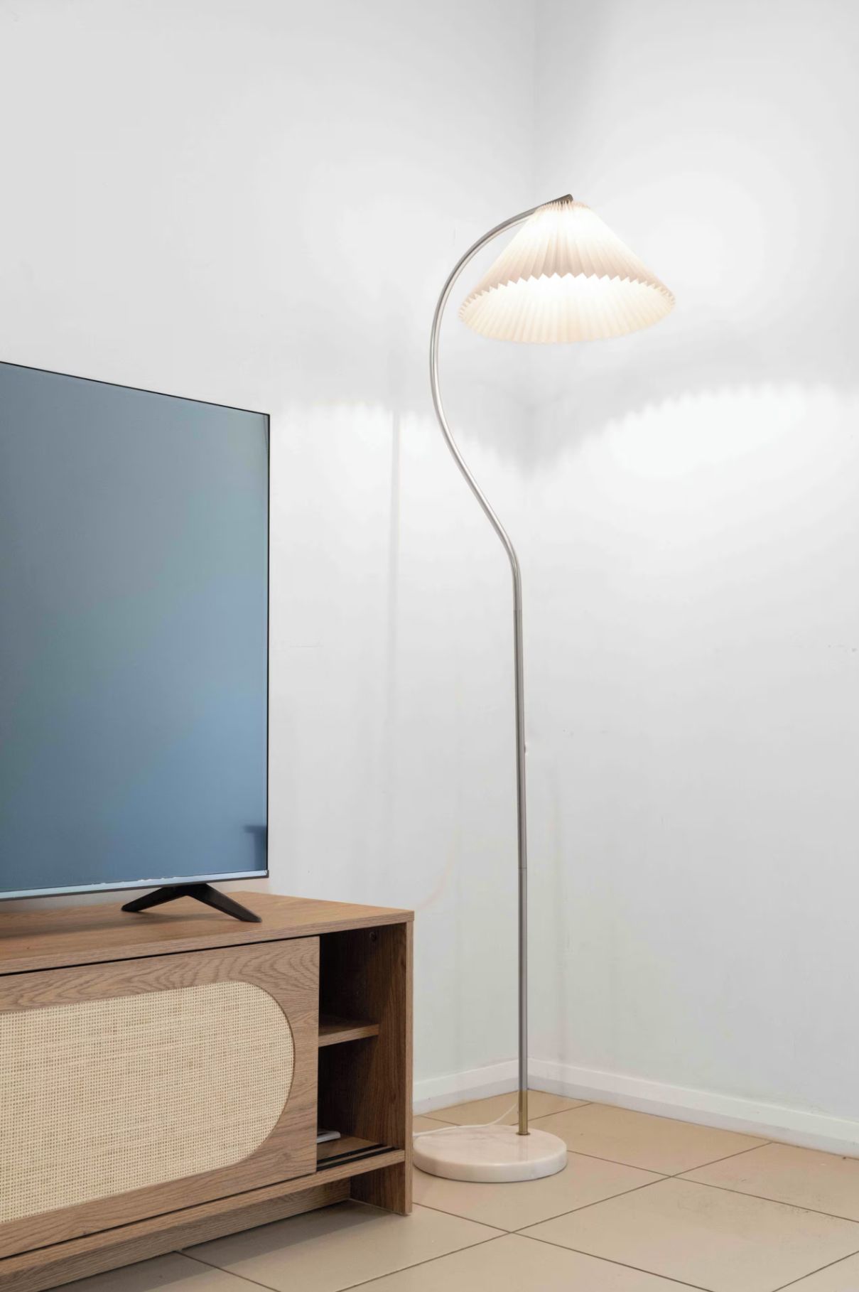 A modern room with a flat-screen TV on a wooden TV stand, a tall floor lamp, and a tiled floor.