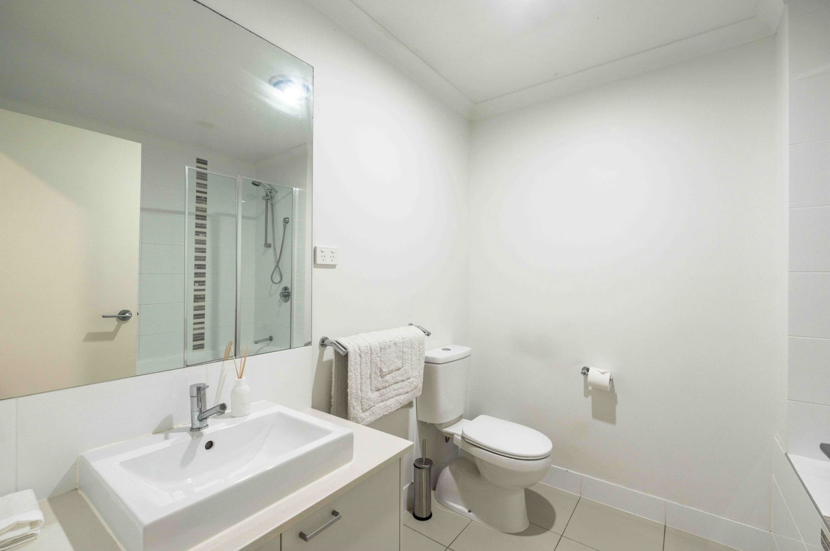 Ein modernes Badezimmer mit Waschbecken, Spiegel, Toilette und Duschkabine aus Glas.