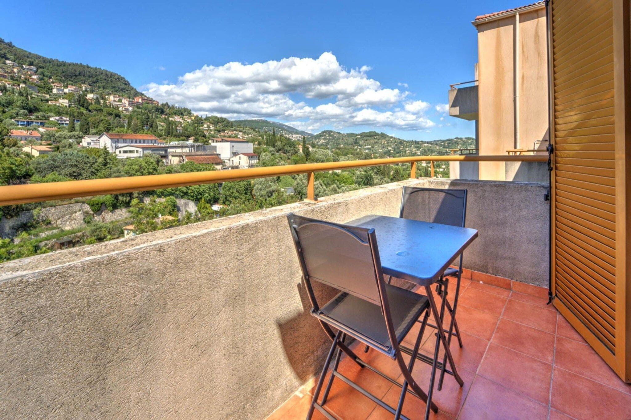 Ein Balkon mit Tisch und Stühlen, der einen Blick auf eine Hügellandschaft mit Häusern bietet.