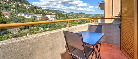 A balcony with a table and chairs, overlooking a hillside with houses.