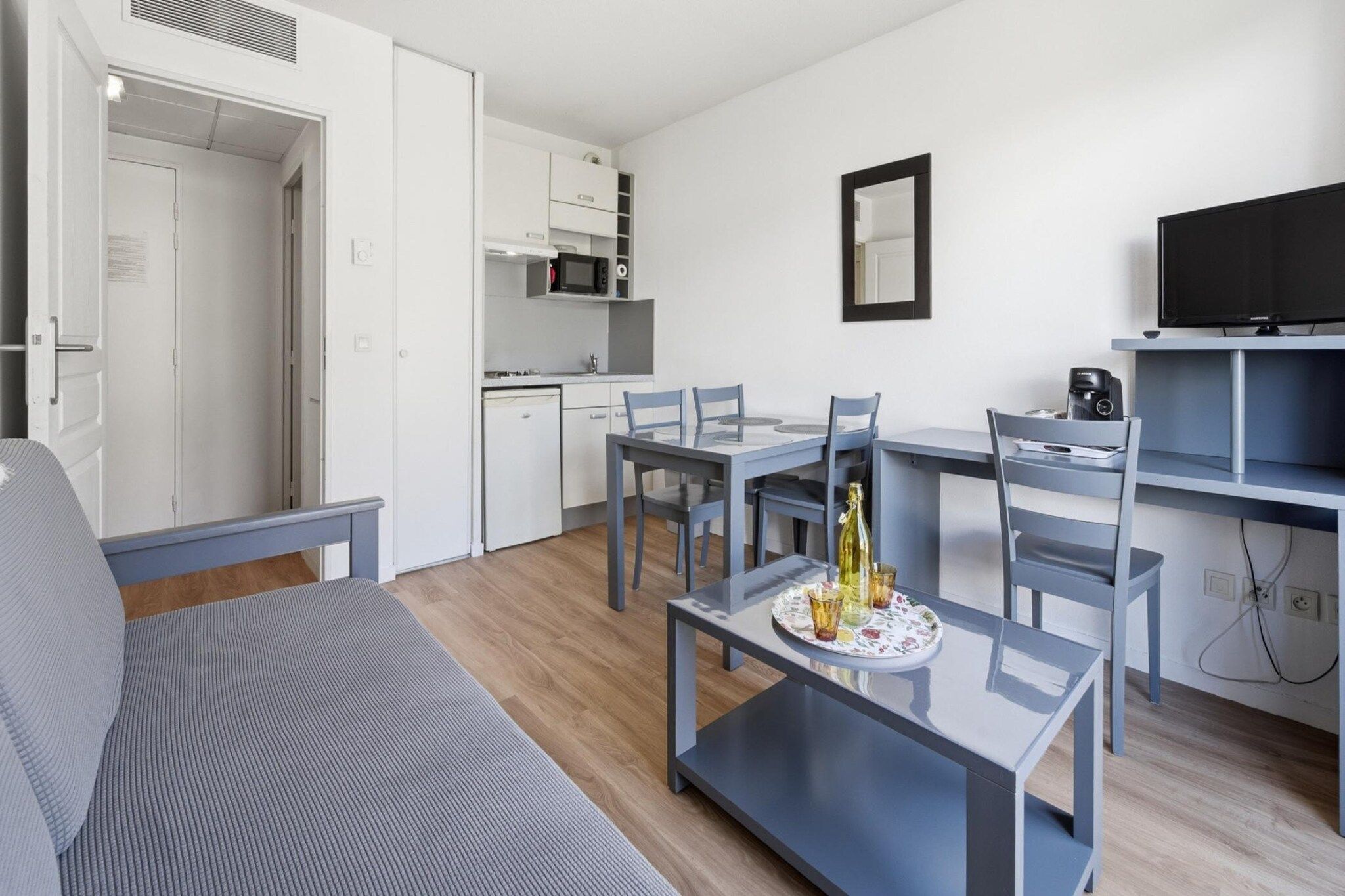 Ein modernes Wohnzimmer mit einer Couch, einem Esstisch mit Stühlen, einer Küchenzeile mit Schränken und einem Fernseher.