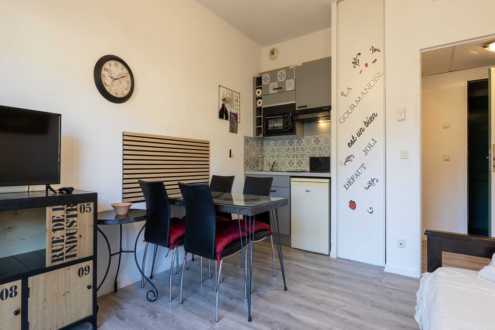 Un espace de vie compact comprenant un coin cuisine, un espace repas avec une table et des chaises, un téléviseur et un lit.