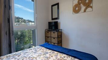 Une chambre à coucher avec un lit, un téléviseur posé sur un meuble, une fenêtre donnant sur un paysage agréable et un élément décoratif mural.