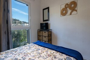 Une chambre à coucher avec un lit, un téléviseur posé sur un meuble, une fenêtre donnant sur un paysage agréable et un élément décoratif mural.