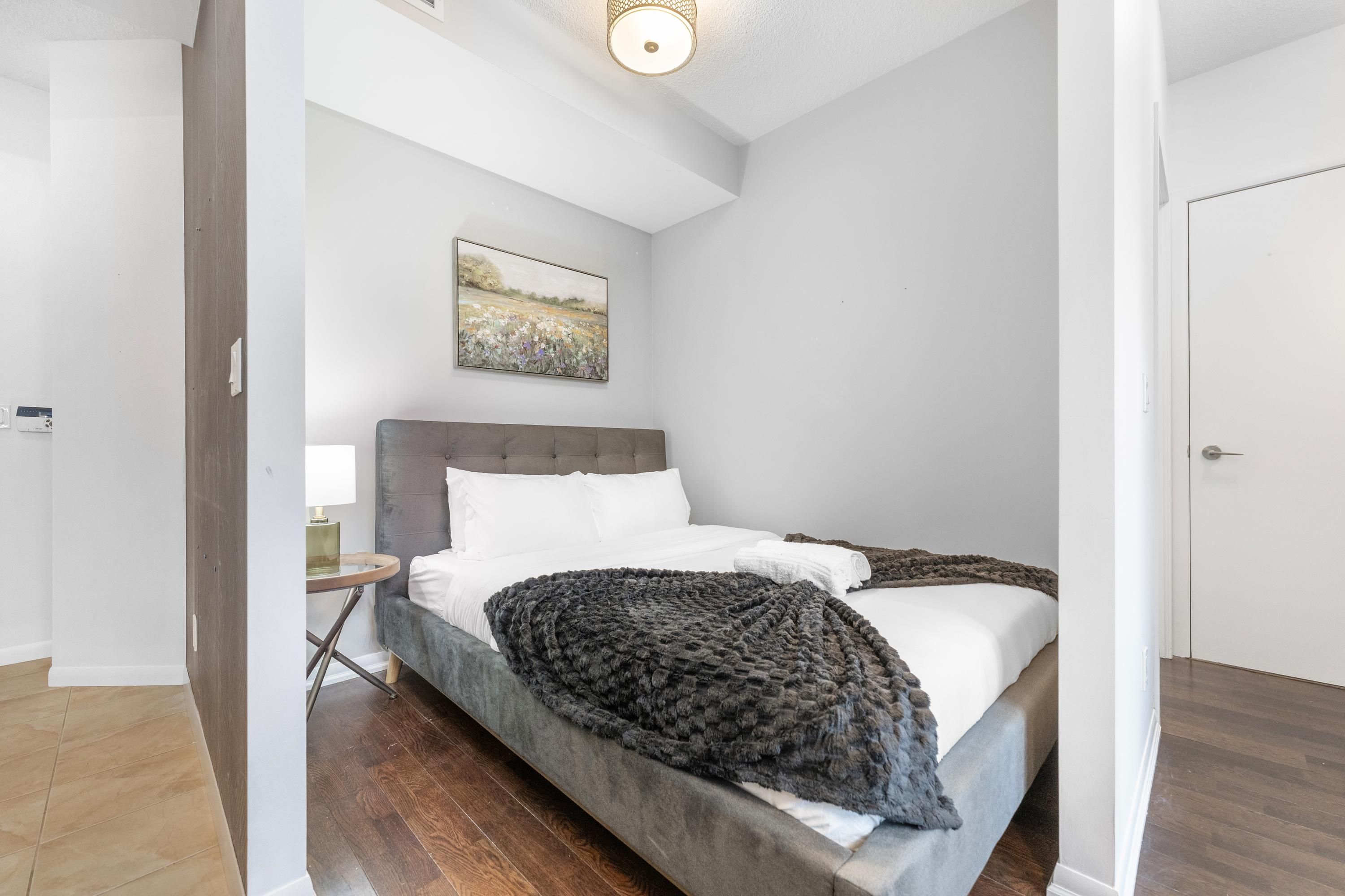 Un dormitorio con una cama, una mesita de noche, una lámpara y un cuadro en la pared.