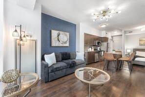Una sala de estar moderna con un sofá gris, una mesa de centro y un comedor con taburetes de bar.