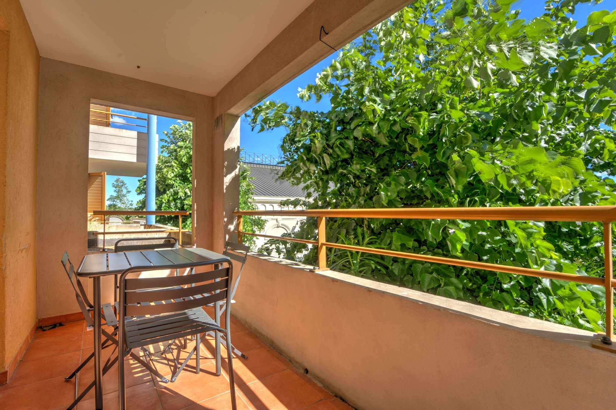 A balcony with a table and chairs, a railing, and a view of greenery and buildings.