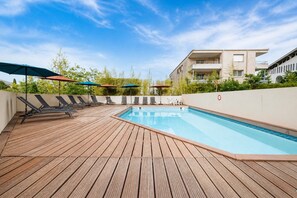 Une terrasse en bois avec une piscine, des chaises longues et des parasols.