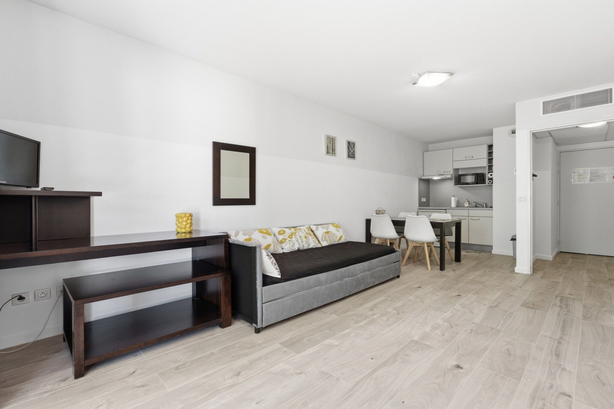 Un salon moderne comprenant un canapé, un téléviseur, une petite table et un coin cuisine.