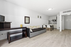 Un salon moderne comprenant un canapé, un téléviseur, une petite table et un coin cuisine.