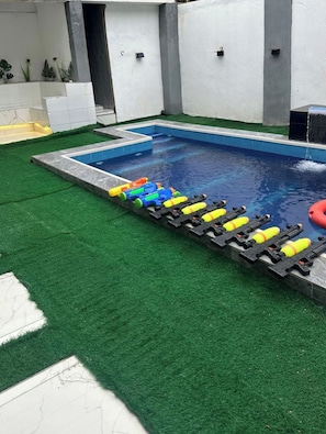 A swimming pool with artificial grass around it and a water slide with colorful water toys. - ORHUE APARTMENT (Benin City)