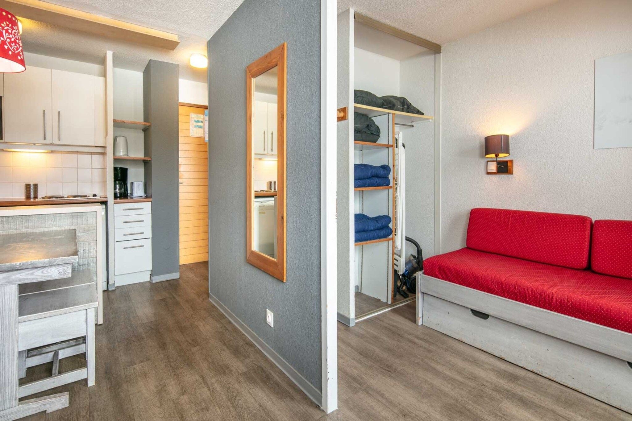 Ein kleiner Wohnbereich mit Küchenzeile, einem roten Sofa, einem Spiegel und einer Regaleinheit.
