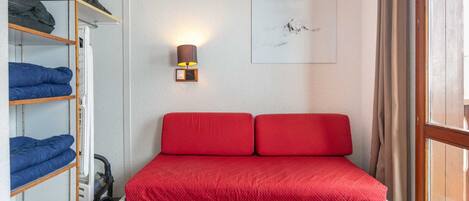 A compact bedroom with a single bed, a wardrobe, a wall-mounted lamp, and a window with curtains.