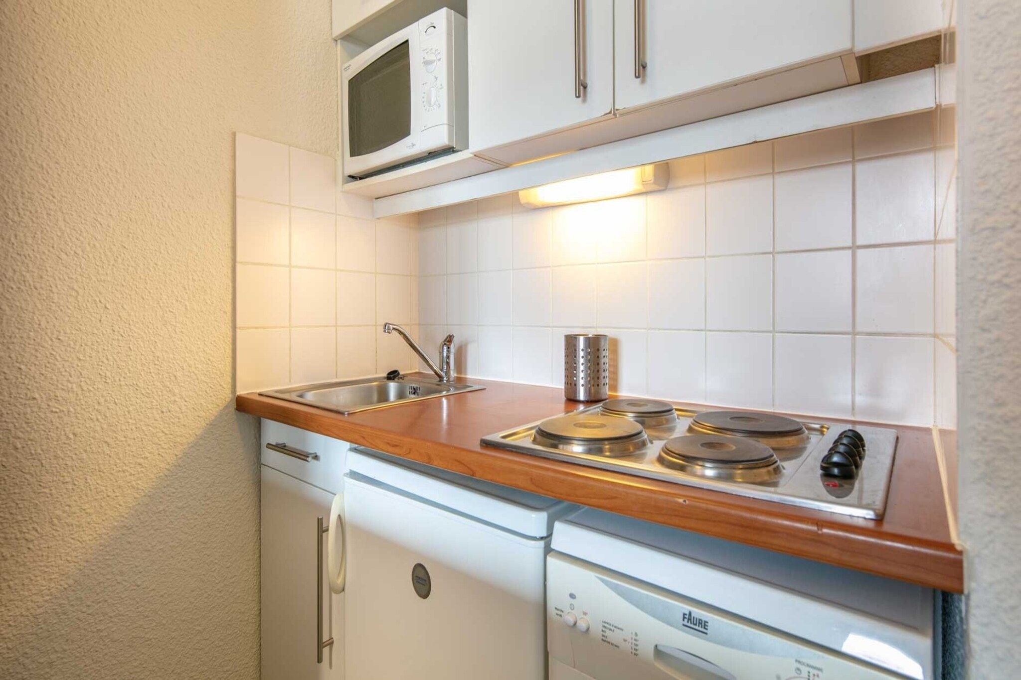 Une petite cuisine équipée d’un four à micro-ondes, d’un évier et d’une cuisinière.